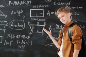 A young student confidently demonstrating geometric formulas on a classroom blackboard.