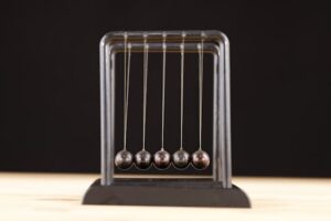 Close-up of a Newton's Cradle resting on a wooden surface against a dark background.