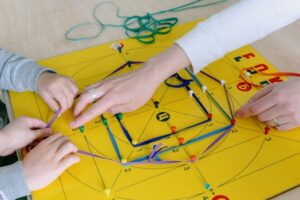 Close-up of hands creating geometric patterns with colorful strings and pins on a board.