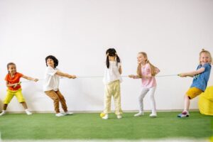 Happy children enjoying a tug of war game indoors, showcasing teamwork and fun.